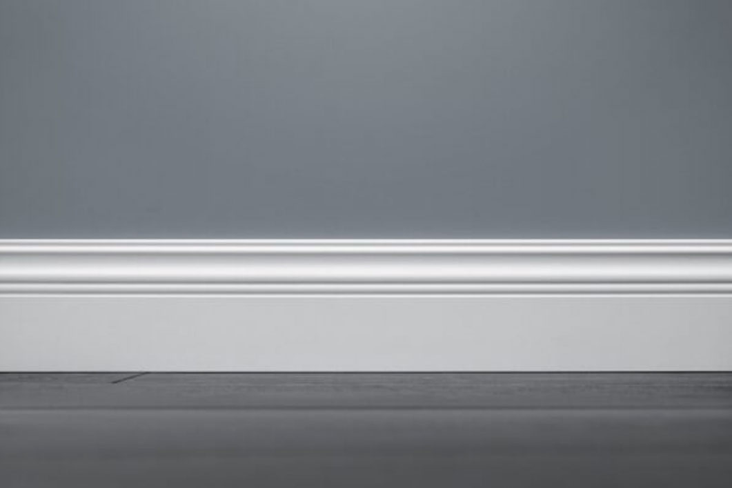 A gray wall with a white baseboard runs horizontally across the image. The floor appears dark and slightly out of focus in the foreground. The baseboard has a simple, clean design with subtle detailing.